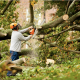 Man in hardhat trimming branches from a fallen tree, by using a chainsaw.